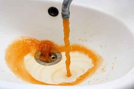 Orange/yellow iron water coming out of the faucet into the sink