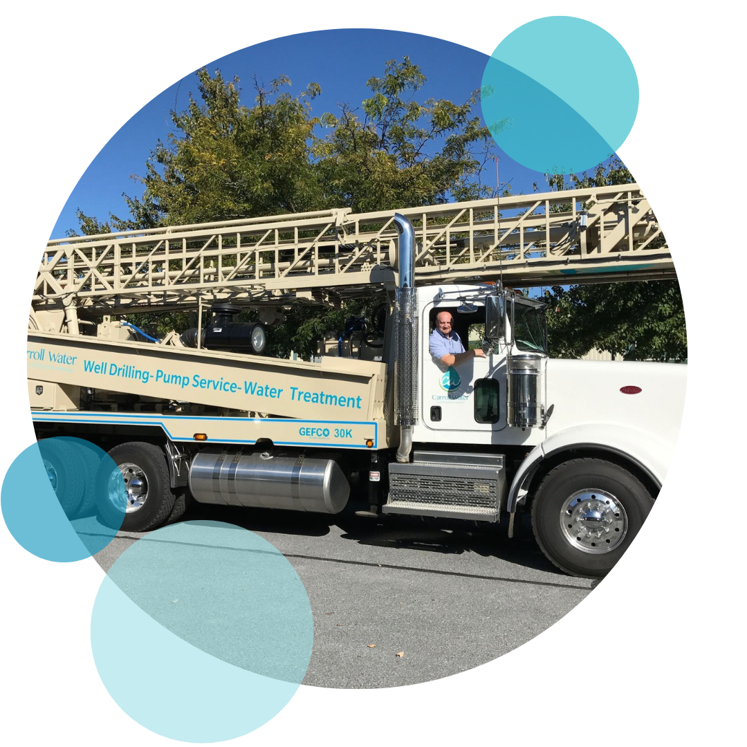 Carroll Water service truck with the words "Well Drilling-Pump Service-Water Treatment" written on the side in blue lettering, while a smiling worker leans out the window of the vehicle.