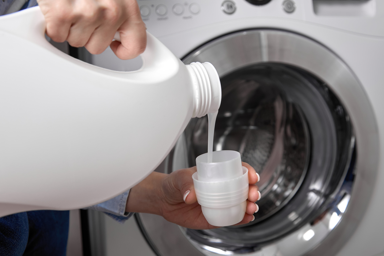 Close-up view of a woman pouring laundry detergent into the bottle cap to measure it, using extra due to hard water issues.