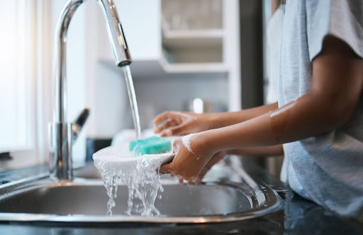 A person using hard water from the kitchen sink to wash dishes.