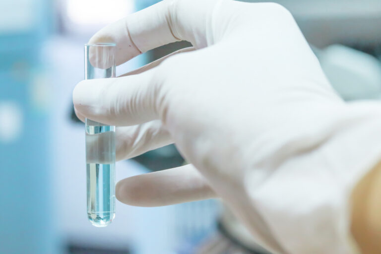A person wearing a white glove holding a glass test tube filled with water for water testing